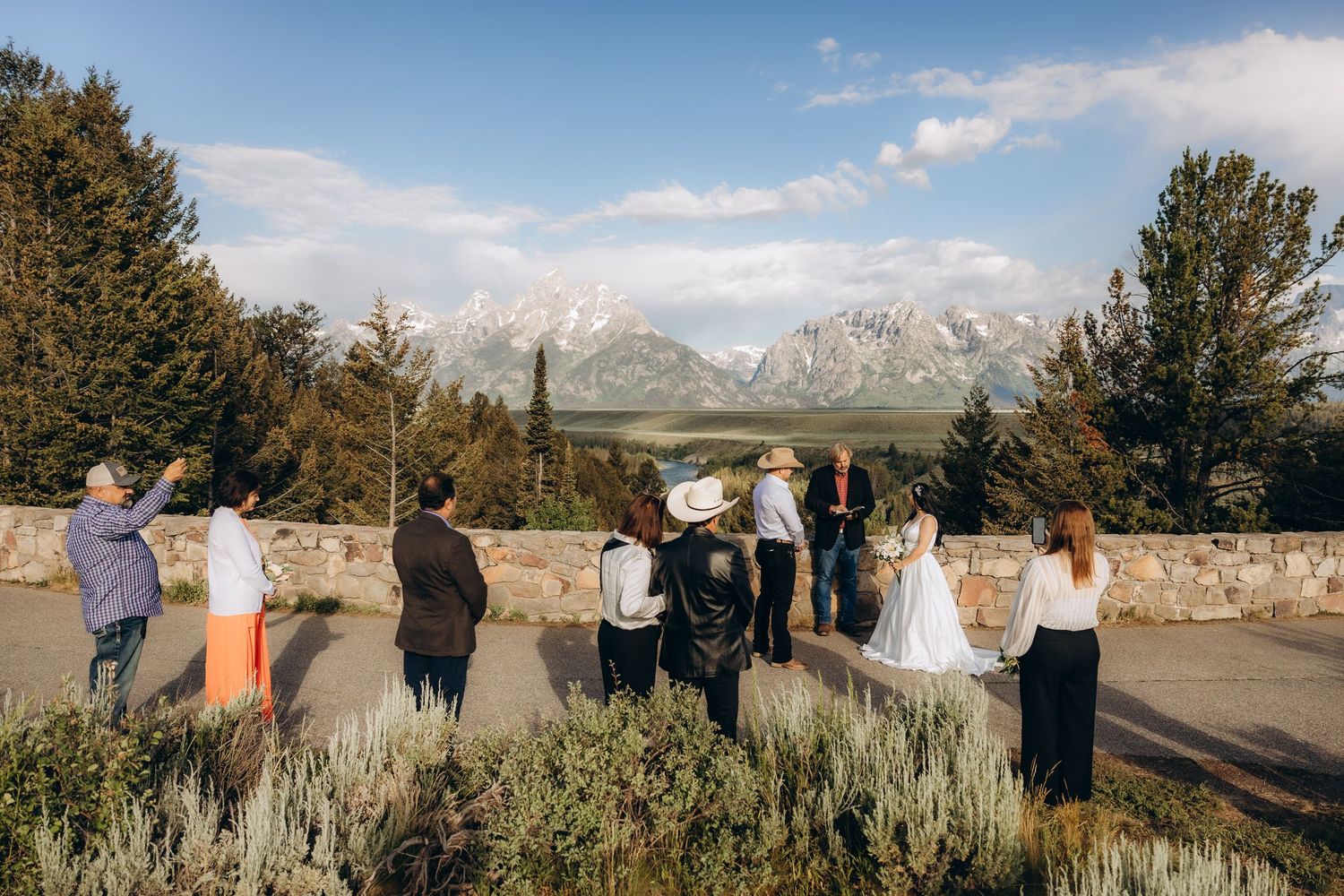 A small outdoor gathering at a scenic overlook with the majestic Grand Teton mountains in the background.