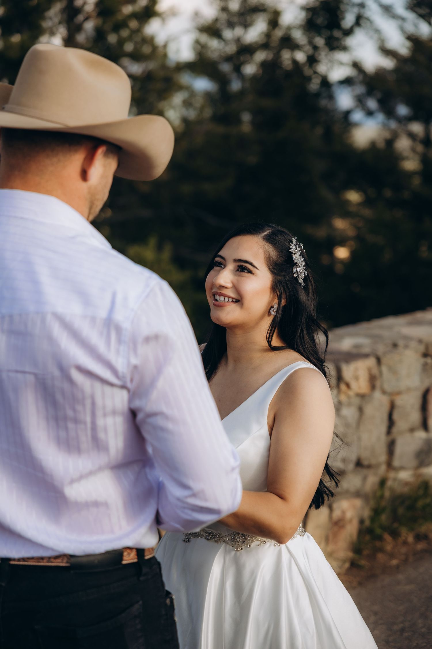 A romantic outdoor wedding moment features a western-themed couple embracing near a stone wall at sunset.