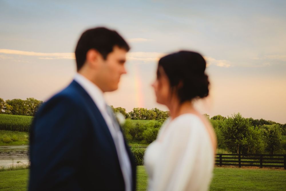 A couple in wedding attire standing outdoors at sunset with lush greenery and shadows creating a romantic atmosphere.