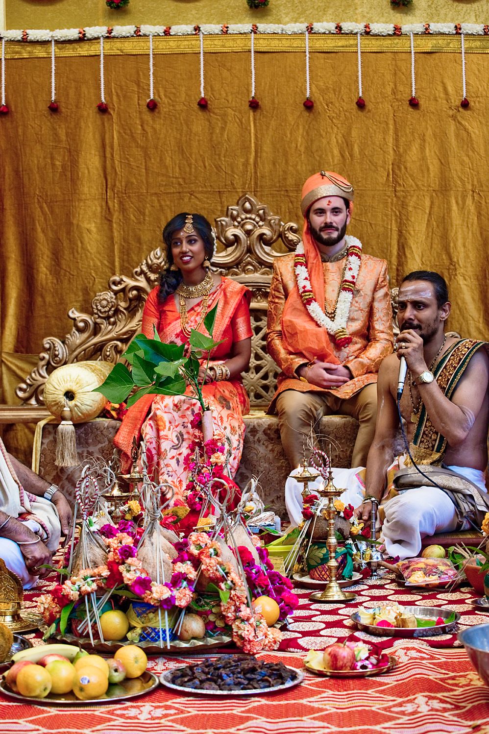 Traditional Indian wedding ceremony with ornate decor, colorful attire, and a feast of fruits and offerings laid out.