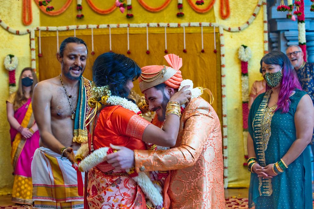 Colorfully dressed people participate in a joyous traditional Indian cultural celebration with festive yellow backdrop.