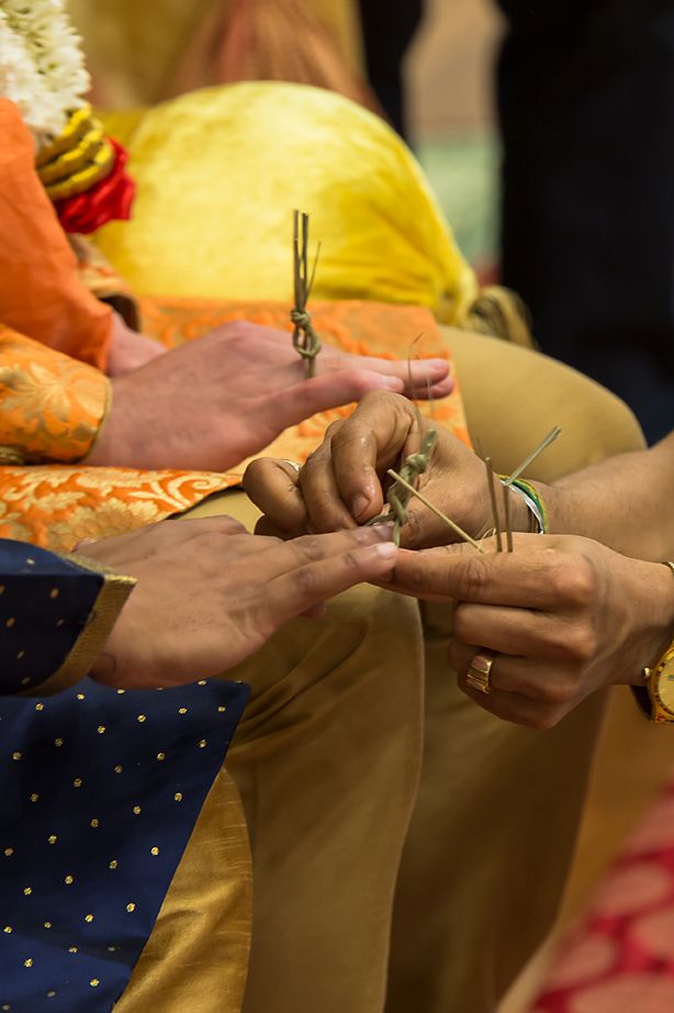 Close-up of hands exchanging wedding rings during traditional Indian ceremony with colorful attire visible.
