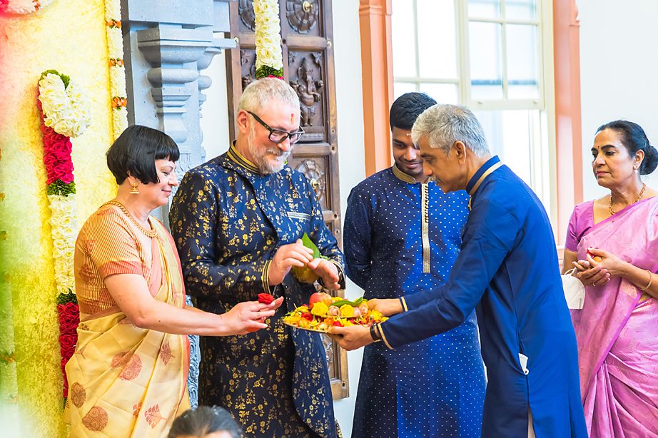 People in traditional Indian attire share a joyful moment exchanging food or gifts outside a colorful building.