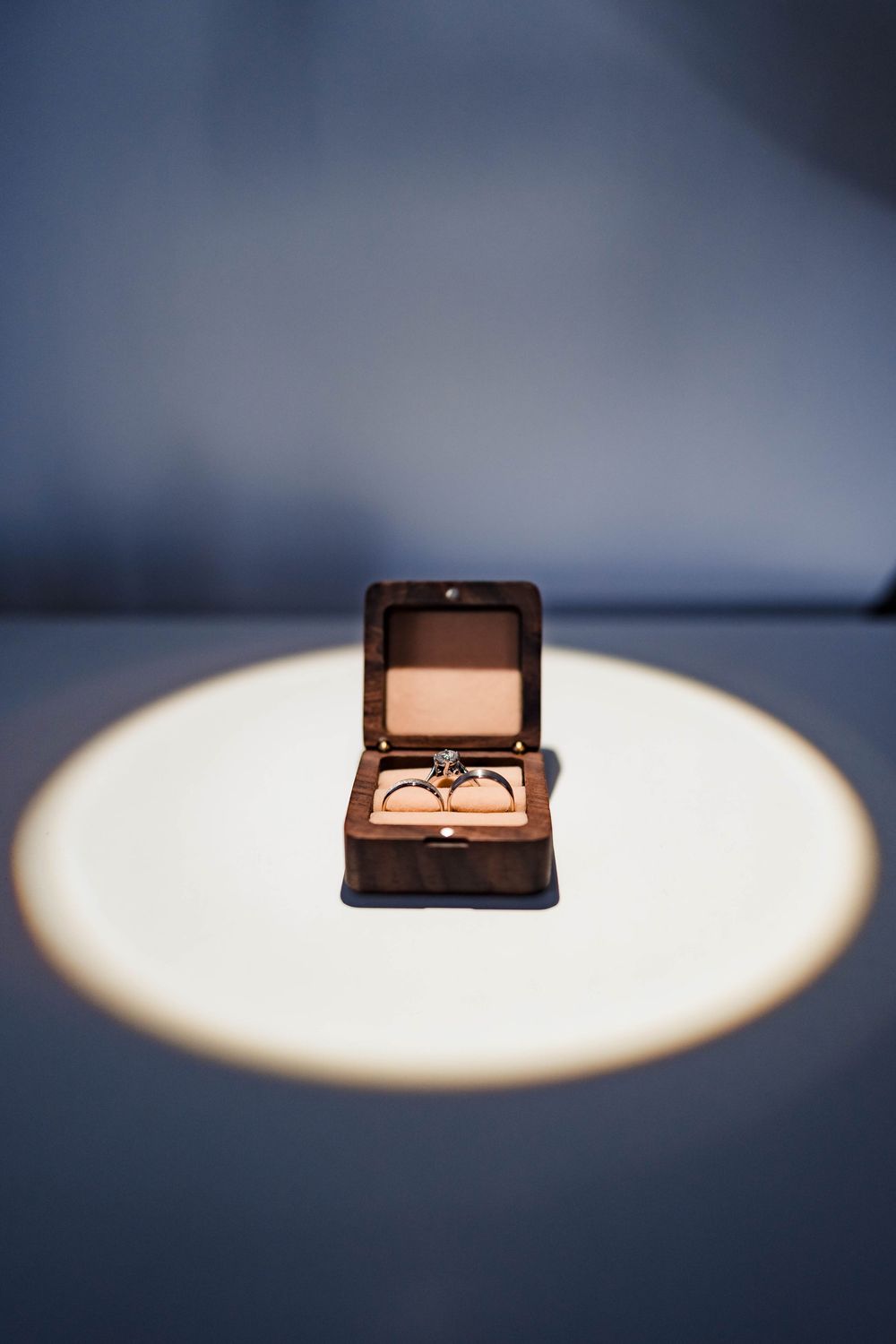 Wedding rings in a brown jewelry box captured in dramatic spotlight.
