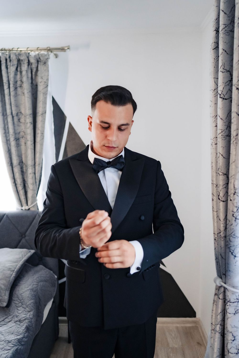 A person in a black tuxedo making final preparations while standing in an elegantly decorated room.