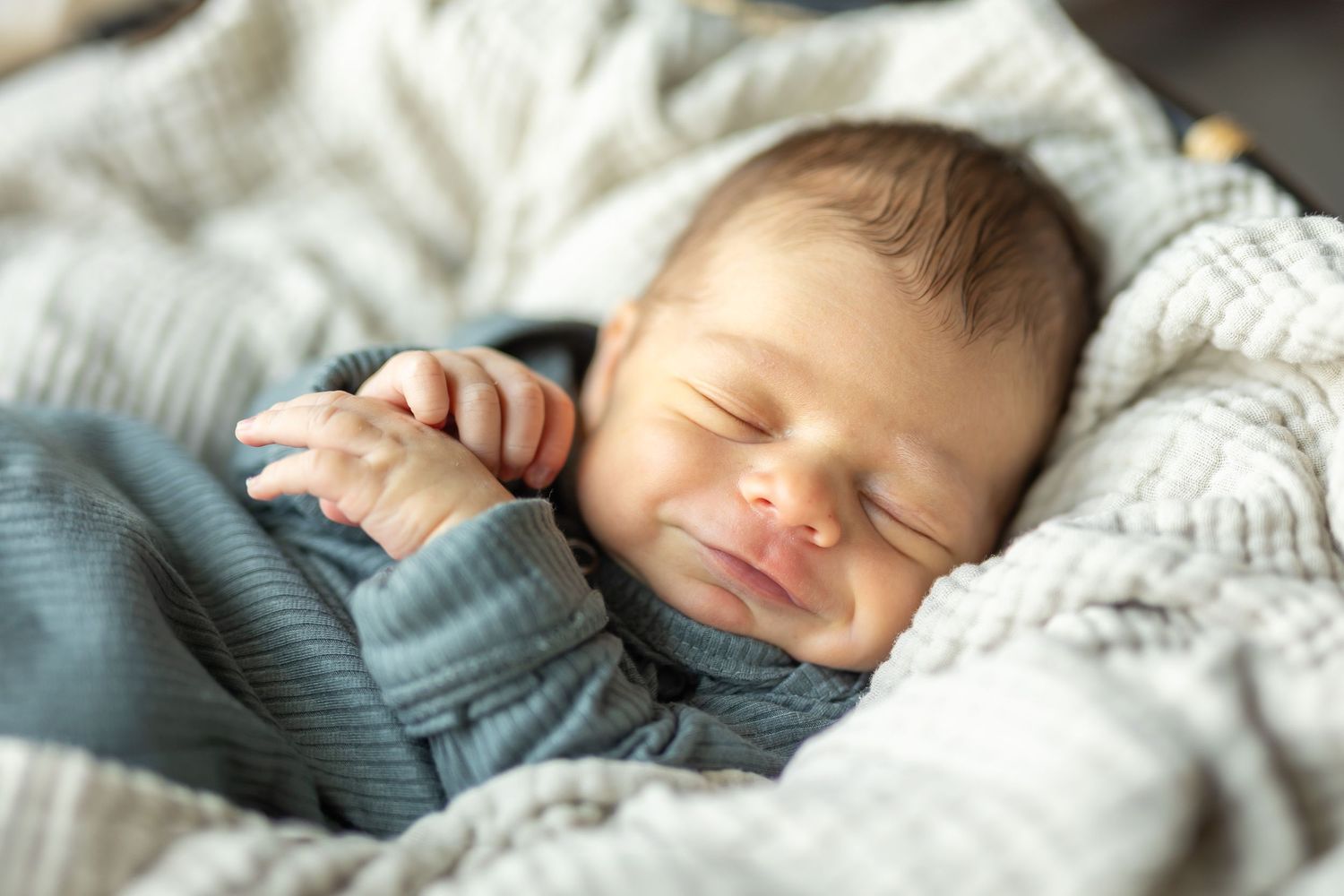 Newborn baby boy snuggled in a basket with a muslin blanket draped under him