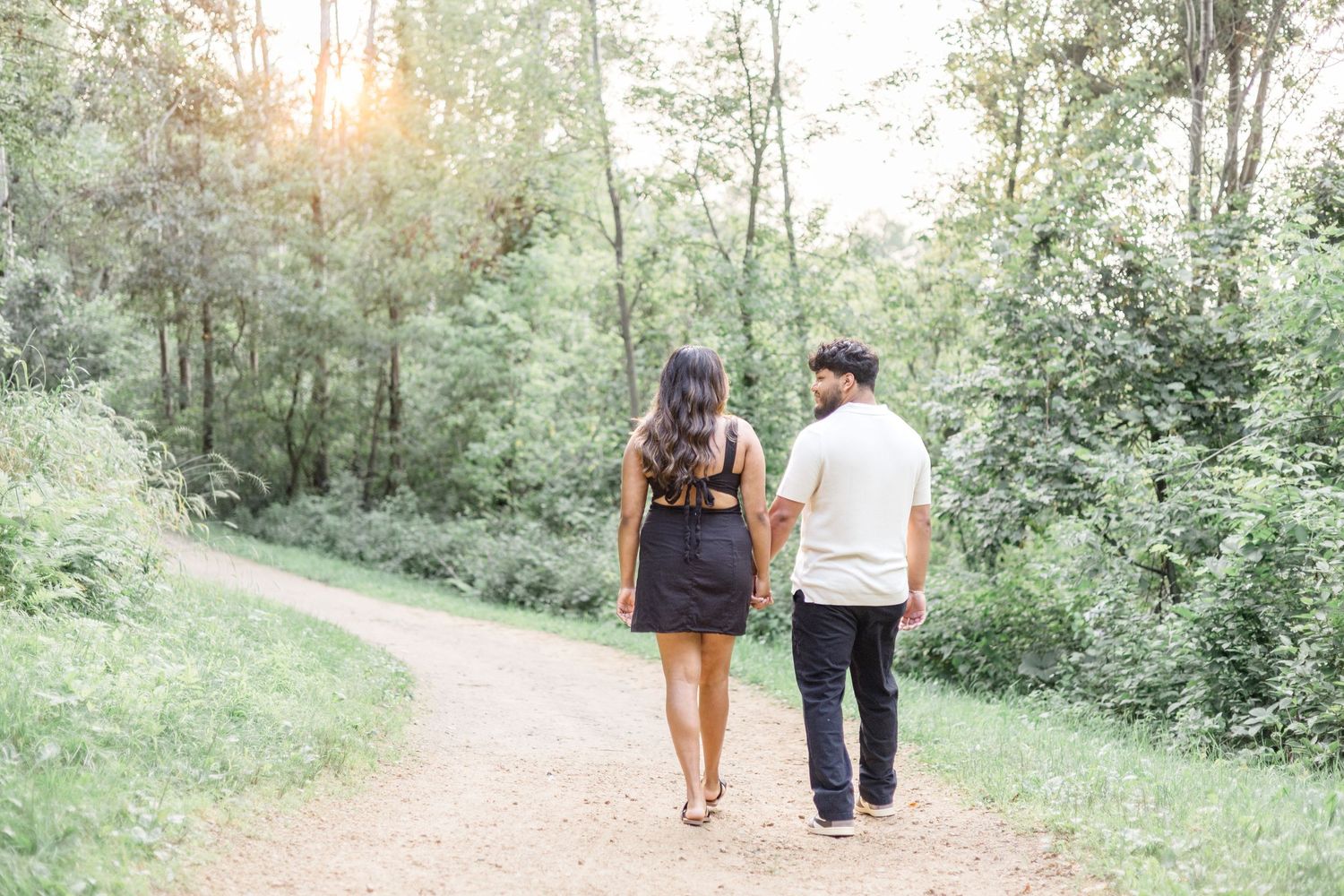 Couple walking together on a scenic wooded trail during golden hour.