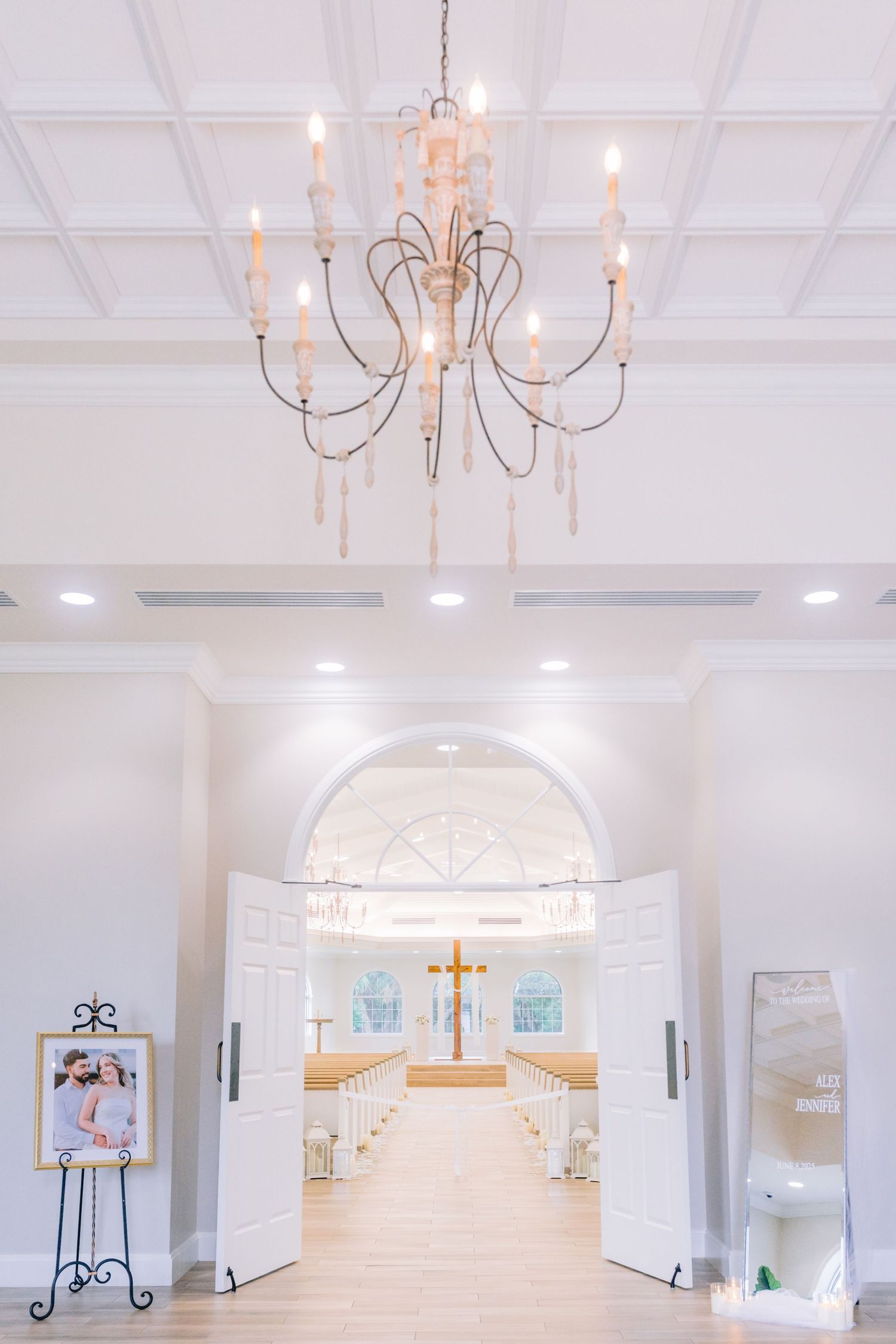 Harborside Chapel, an Elegant interior white with grand chandelier, a vaulted ceiling, and arched doorway leading to a cross-adorned altar.