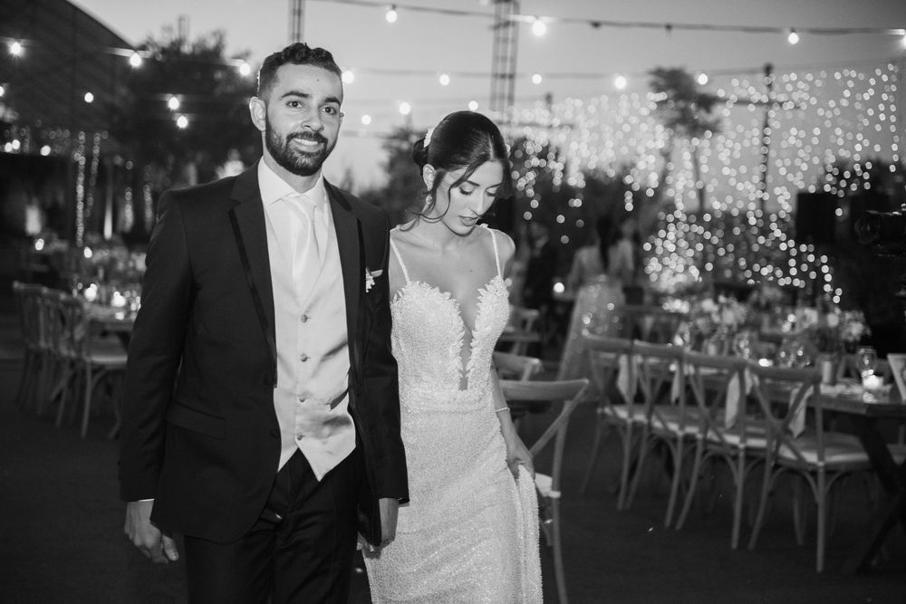 Newlyweds walk through outdoor reception venue decorated with hanging fairy lights.