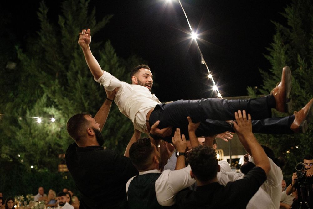 Wedding guest lifted in celebration by crowd during outdoor nighttime reception.