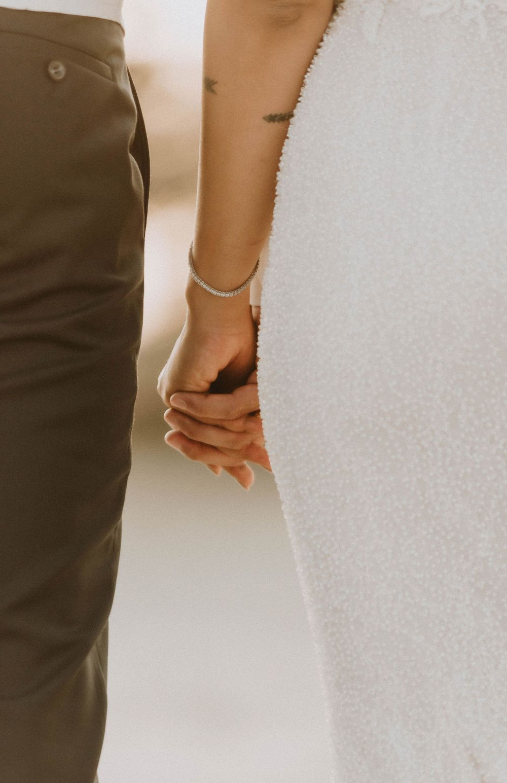 Close-up of couple holding hands, showing a delicate bracelet against wedding attire.
