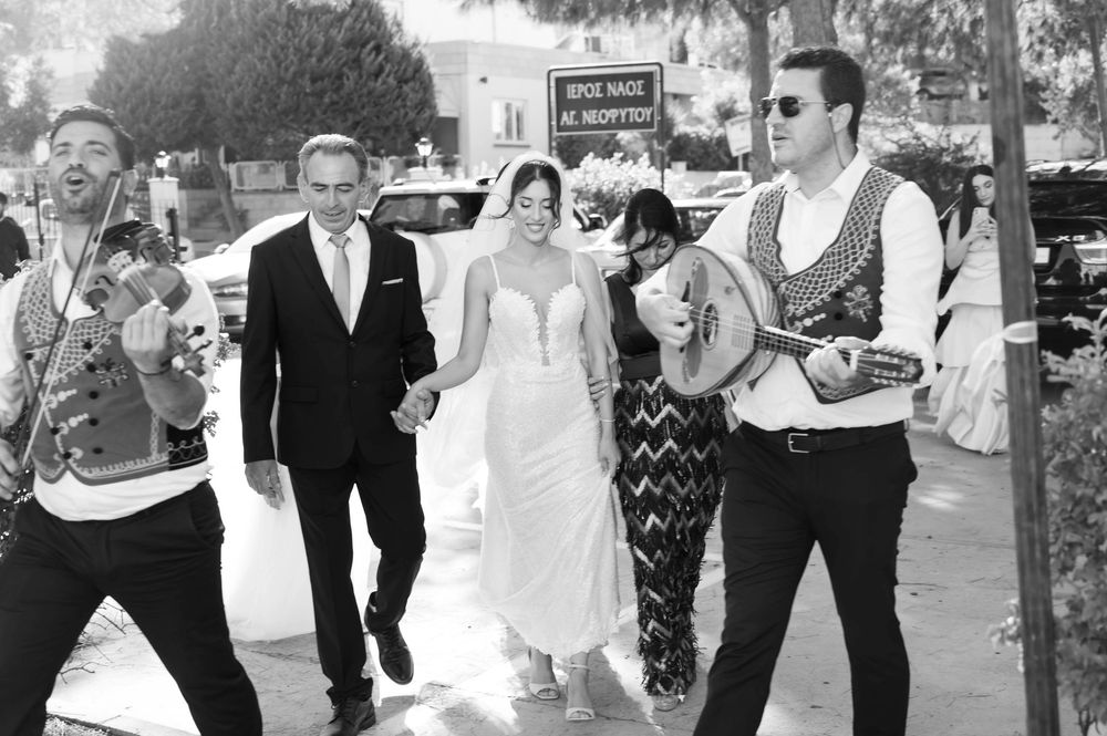 Black and white street scene of wedding party walking with musician in vintage style.