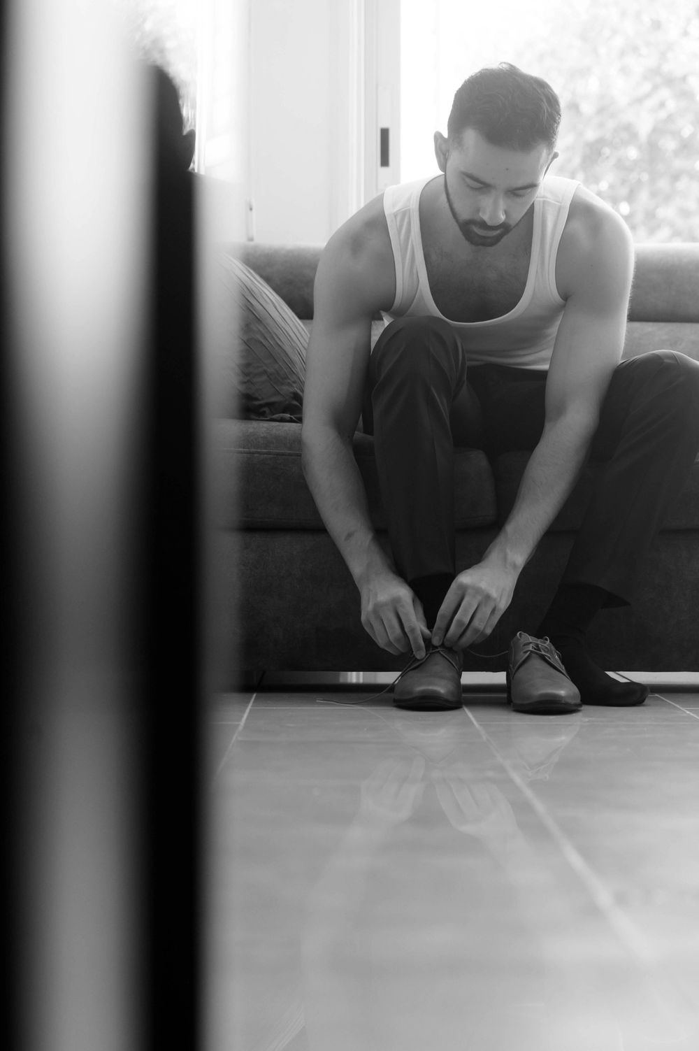 Black and white photo of person sitting on couch tying dress shoes.