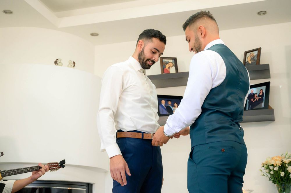 Two people in formal attire inspect a detail on wedding attire before the ceremony.