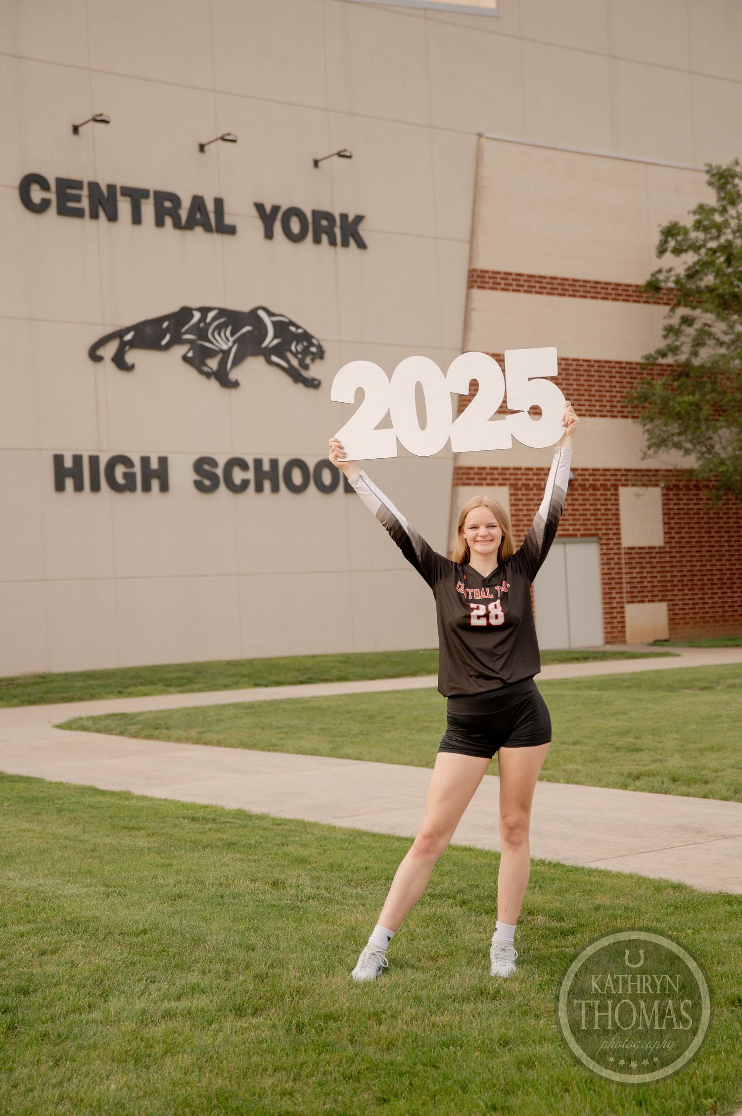 Student athlete in black uniform cheers while holding Class of 2025 sign outside Central York High School entrance.