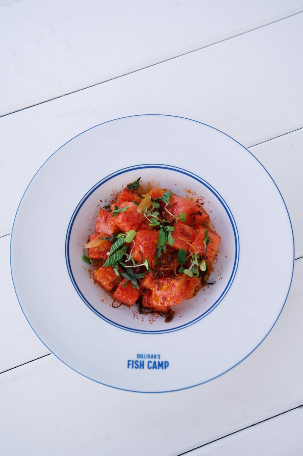 Fresh poke bowl with diced salmon and herbs on a white plate with blue trim.