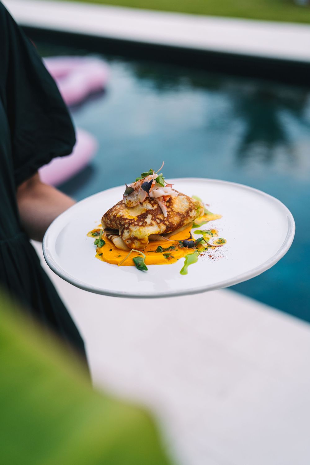 Elegant plated dish with seared protein and microgreens against pool background.