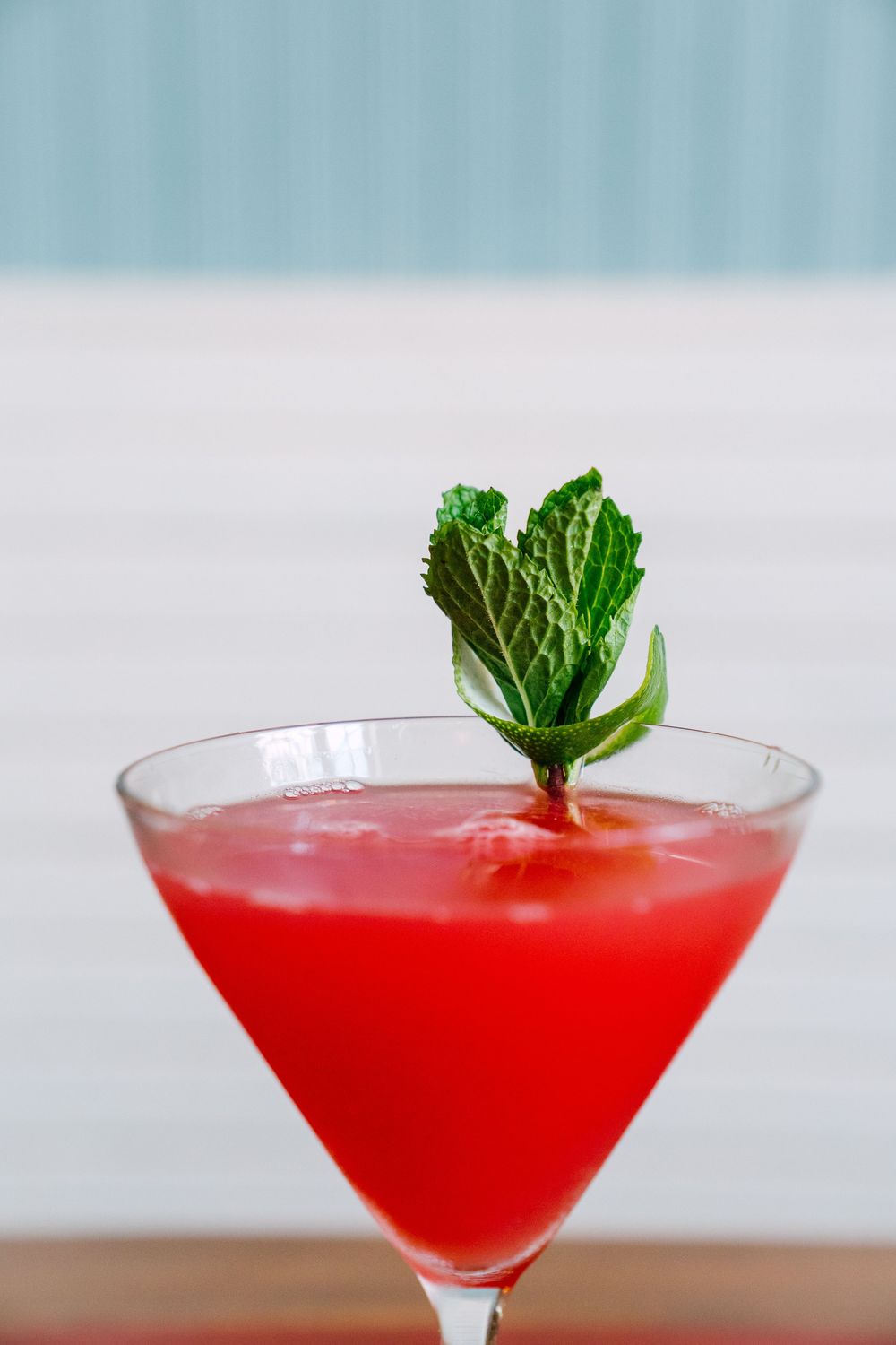 Red martini cocktail garnished with fresh mint leaf in a triangular glass.
