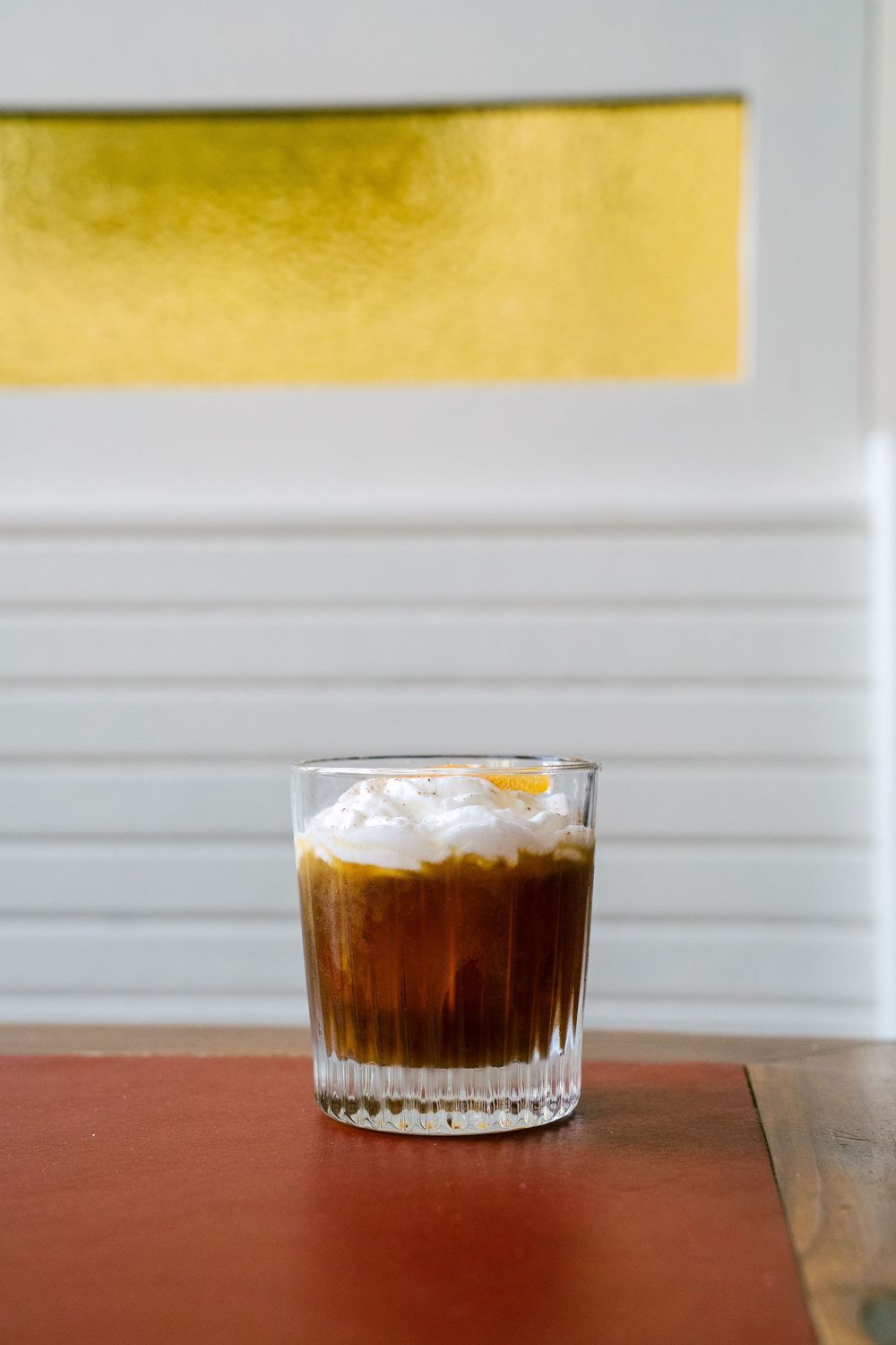 Cold brew coffee with foam served in a textured glass on a wooden surface.