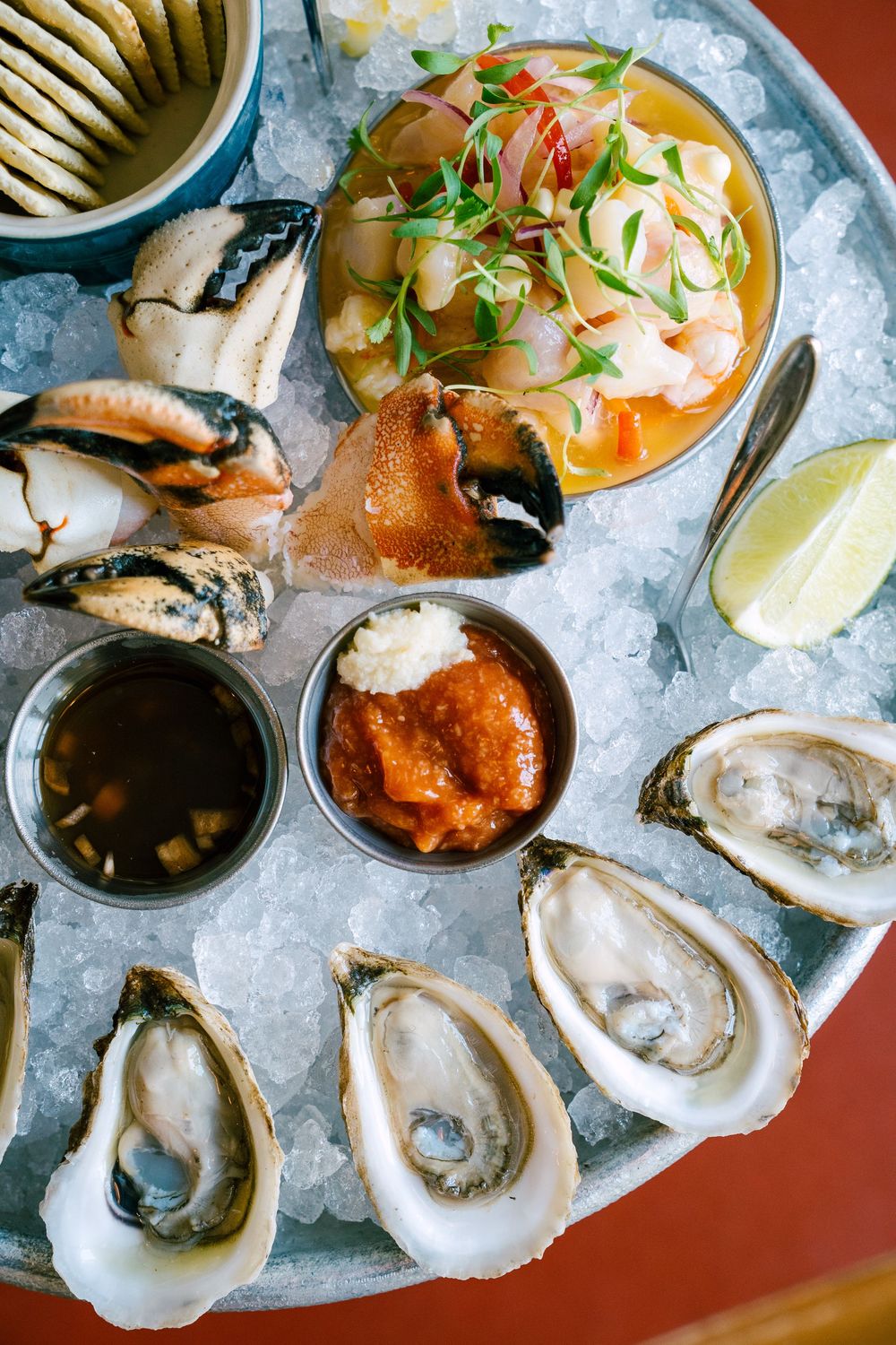 Fresh oysters on ice with shrimp cocktail and sauces served on a red table.