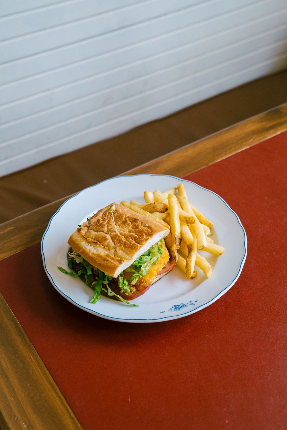 Classic sandwich with french fries served on a white plate against a red surface.