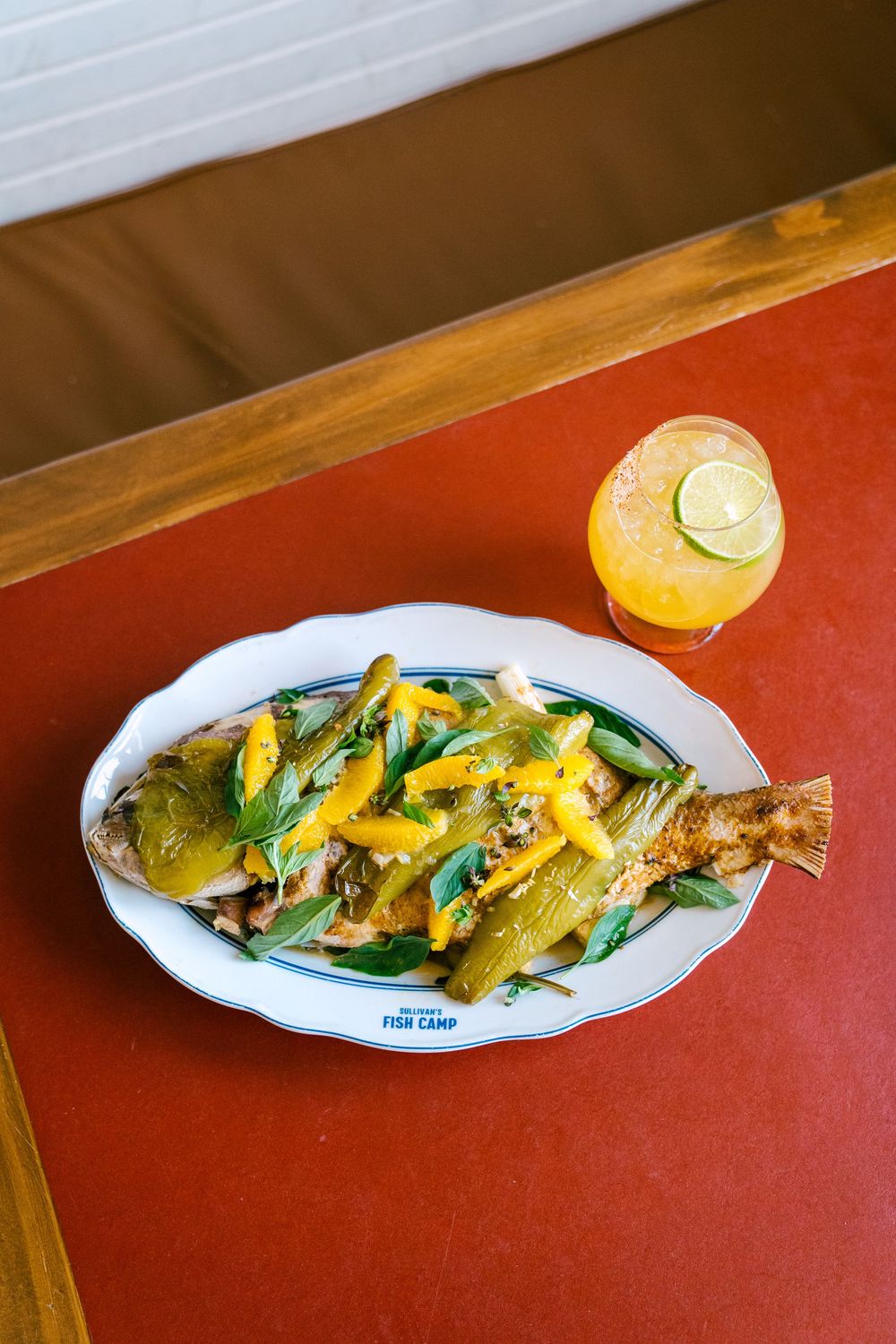 Whole grilled fish with fresh herbs and lemon garnish served on a white platter.