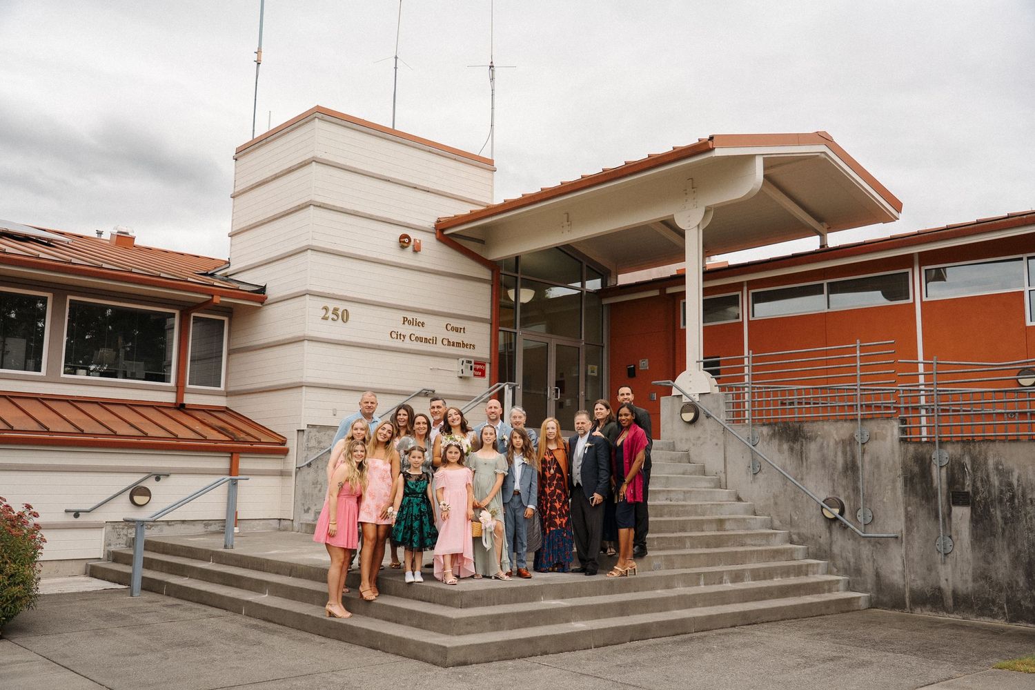 A group of people stands on the front steps of a modern building with orange walls and white accents.