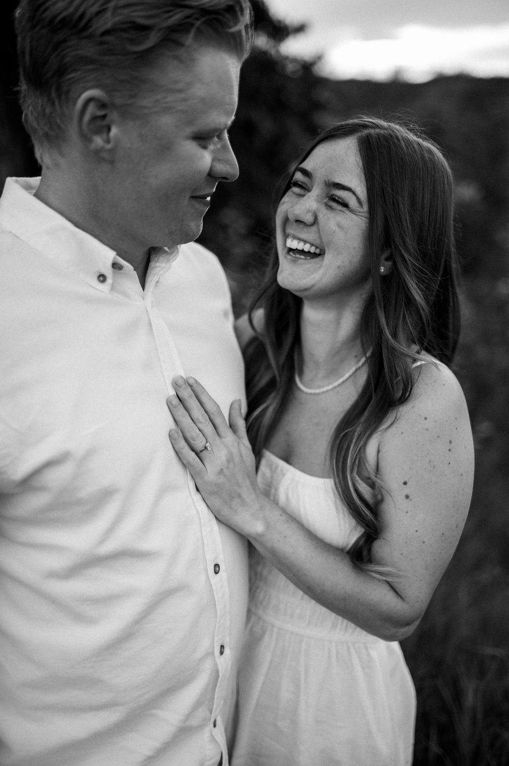 A romantic couple shares joyful laughter together outdoors in black and white portrait series.
