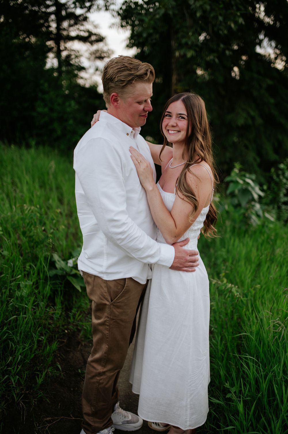 A romantic couple embraces in a lush green field during a summer photoshoot.