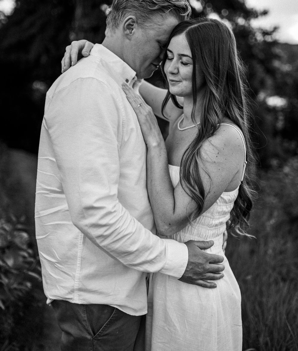 A romantic black and white portrait of a couple embracing in an intimate moment outdoors.