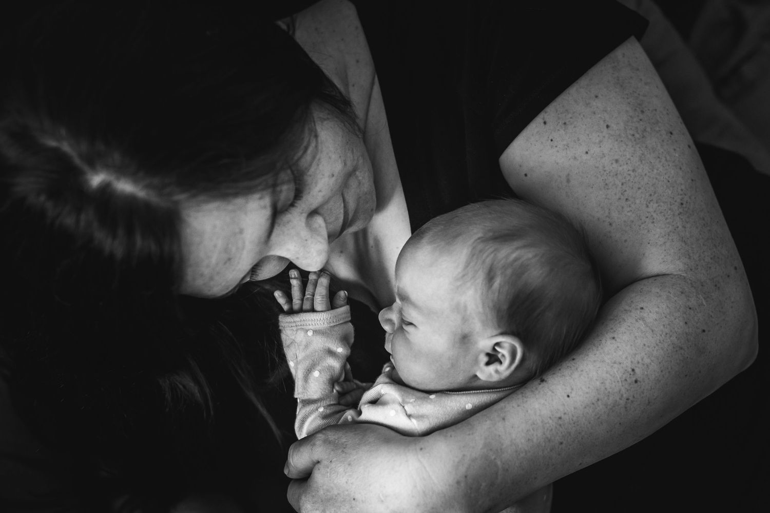 A tender black and white moment shared between parent and infant lying together in intimate closeness.