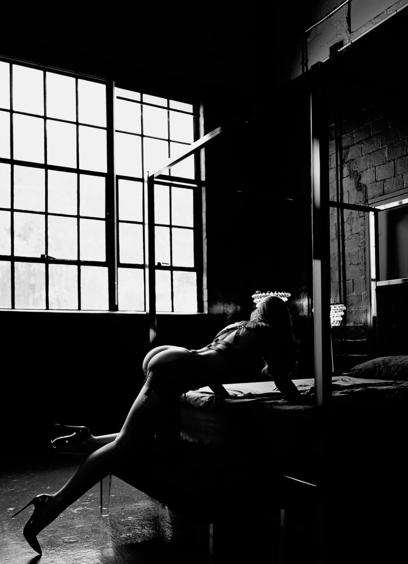 In dim lighting, a figure rests against soft bedding in an intimate pose.