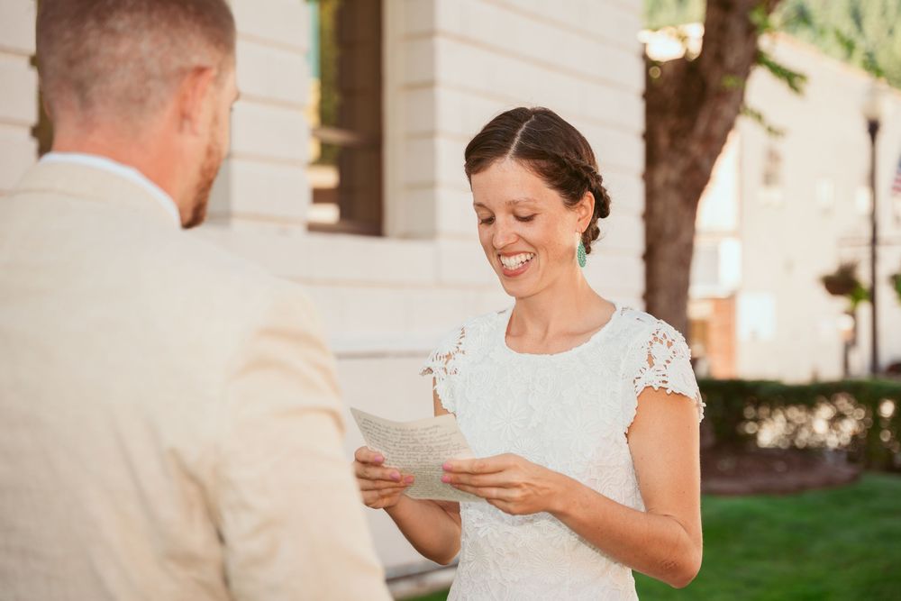 Person in white lace dress reading from paper outdoors.