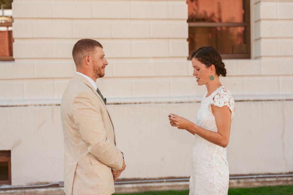 Wedding couple exchanges vows on lawn in front of classic white building.