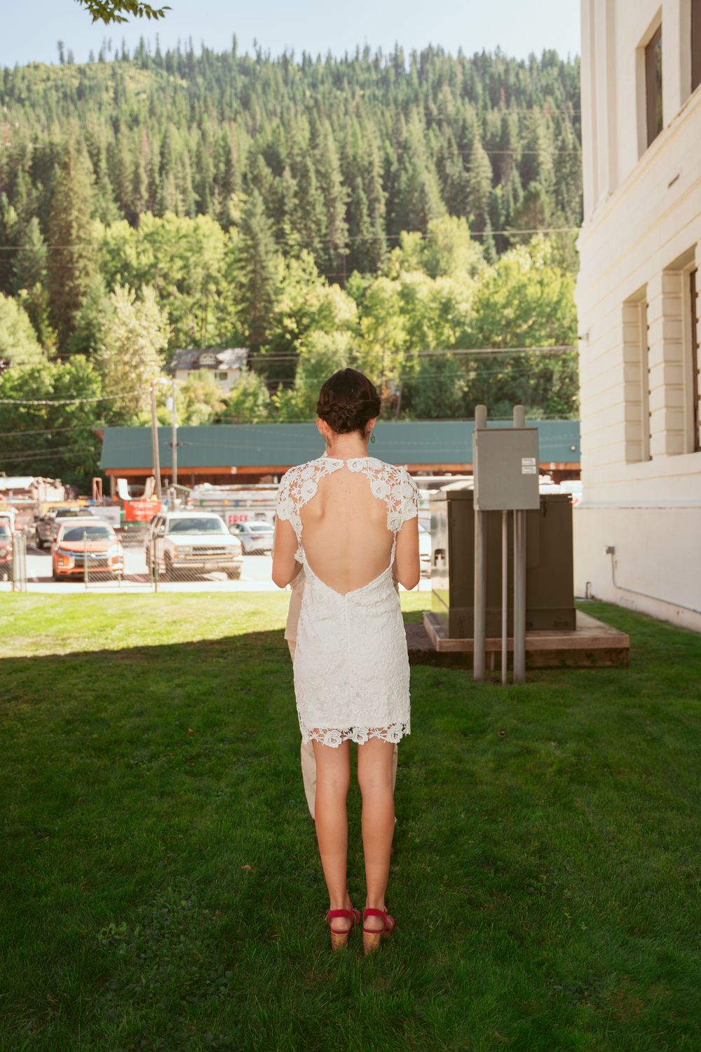 A backless lace wedding dress shown against a mountain landscape backdrop.