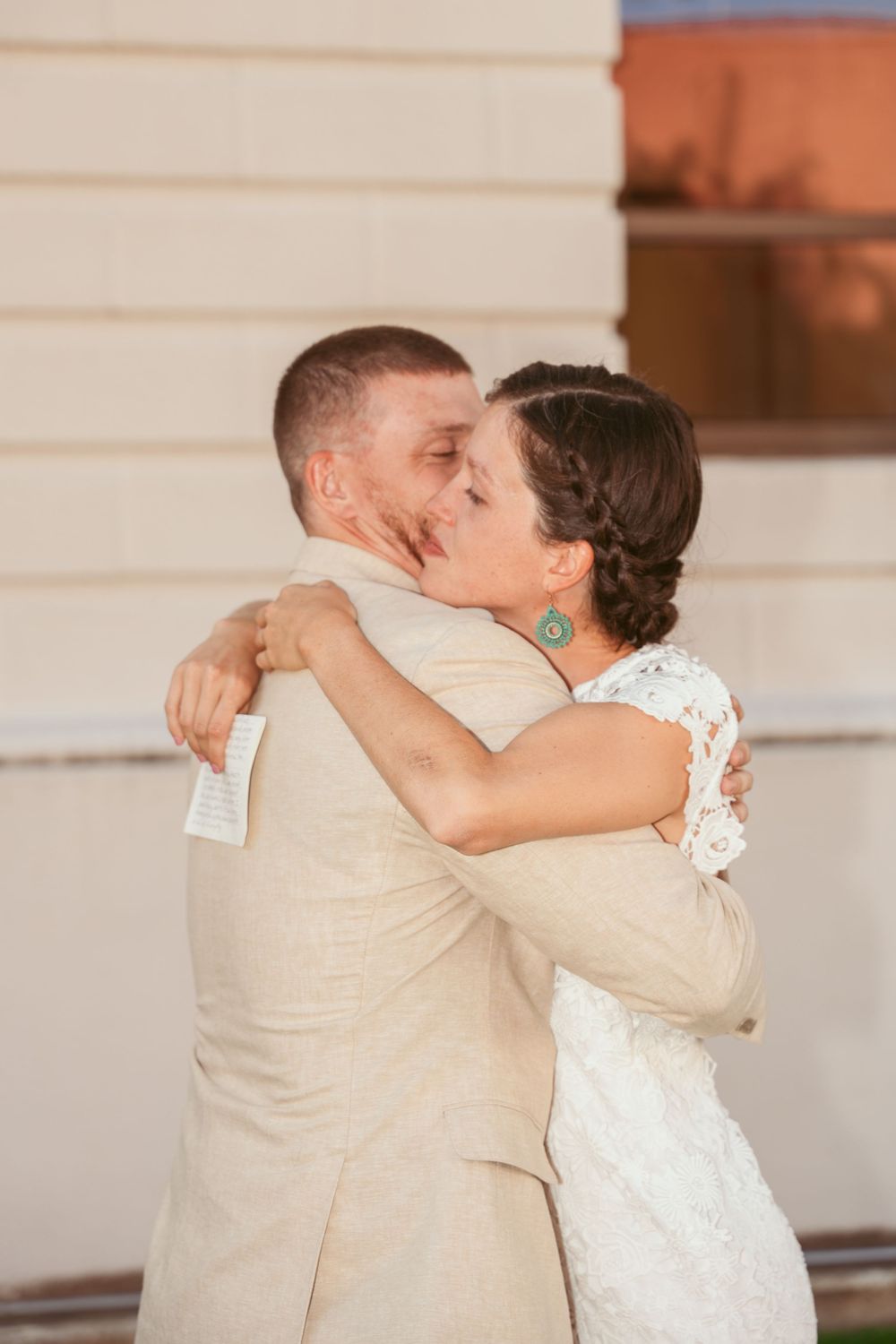A romantic embrace between newlyweds wearing beige and white attire at their wedding celebration.