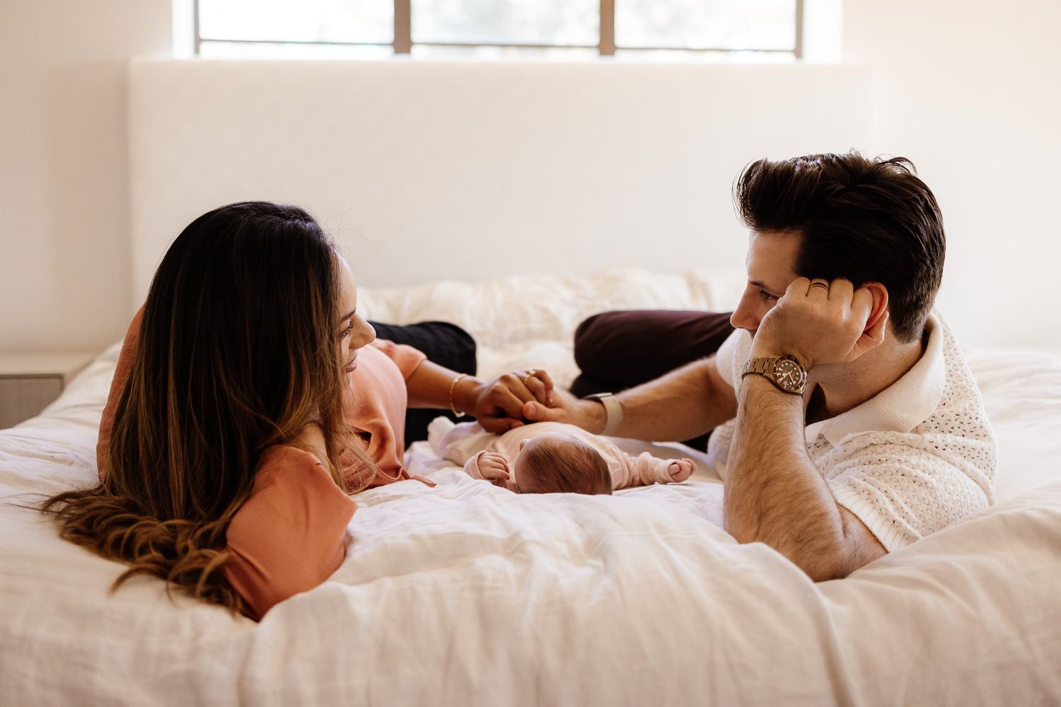 Parents lay on their bed with baby in-between during their newborn photo session in the Bay Area