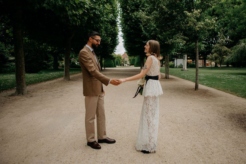 Bride and groom holding hands and facing each other on a serene tree-lined path in Paris.