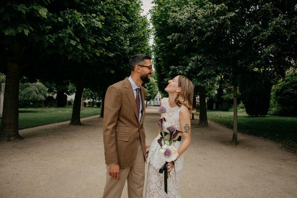 Bride and groom smiling at each other while walking along a lush tree-lined path in Paris.