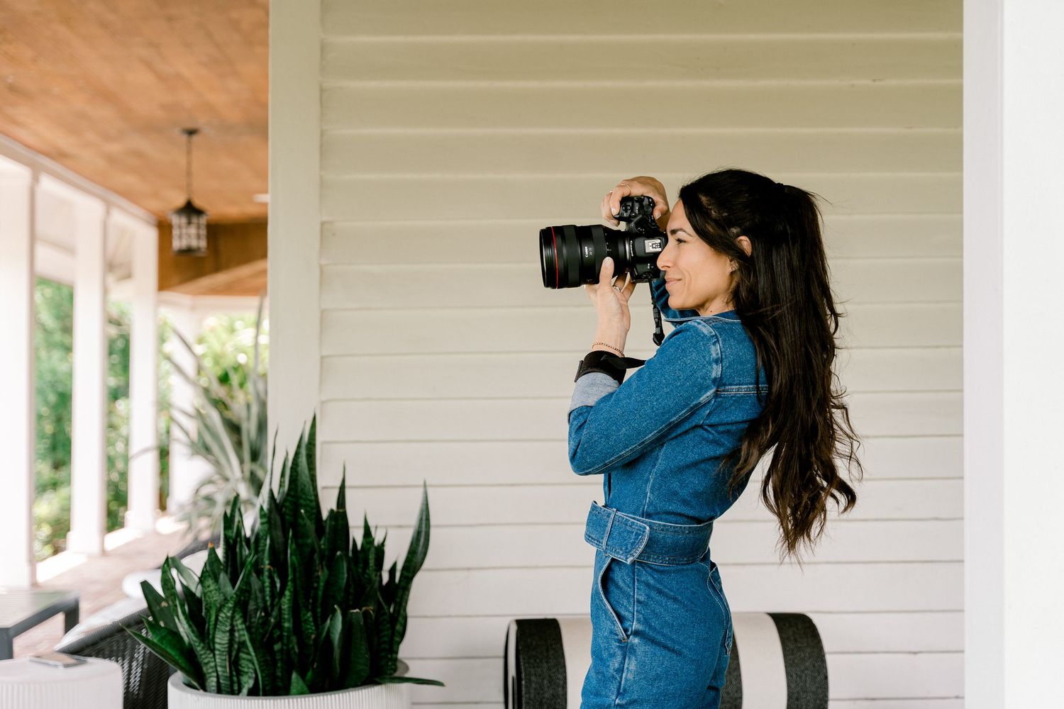 Professional photographer in denim shirt taking photos on outdoor wooden porch.