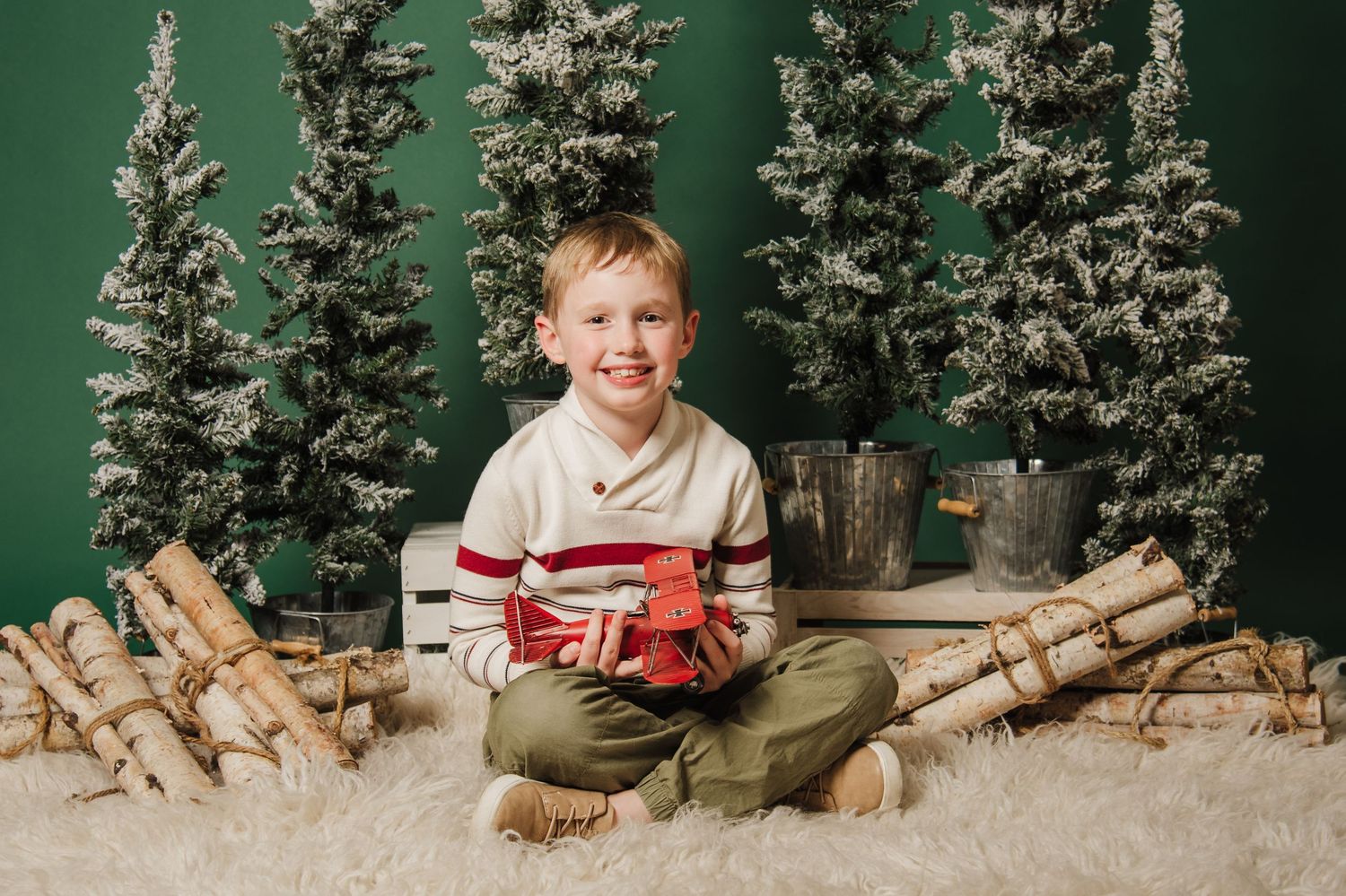 A child sits with a wrapped gift among snow-covered trees against a green backdrop.