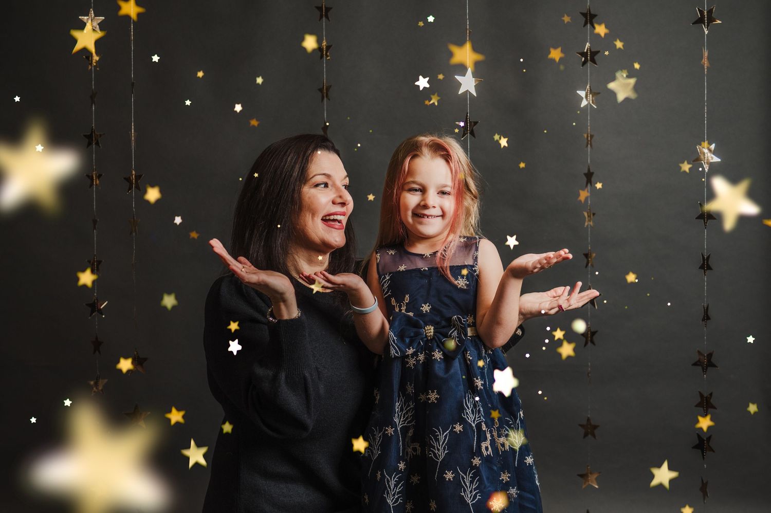 Magical photo session with hanging gold stars and twinkling lights against dark background.