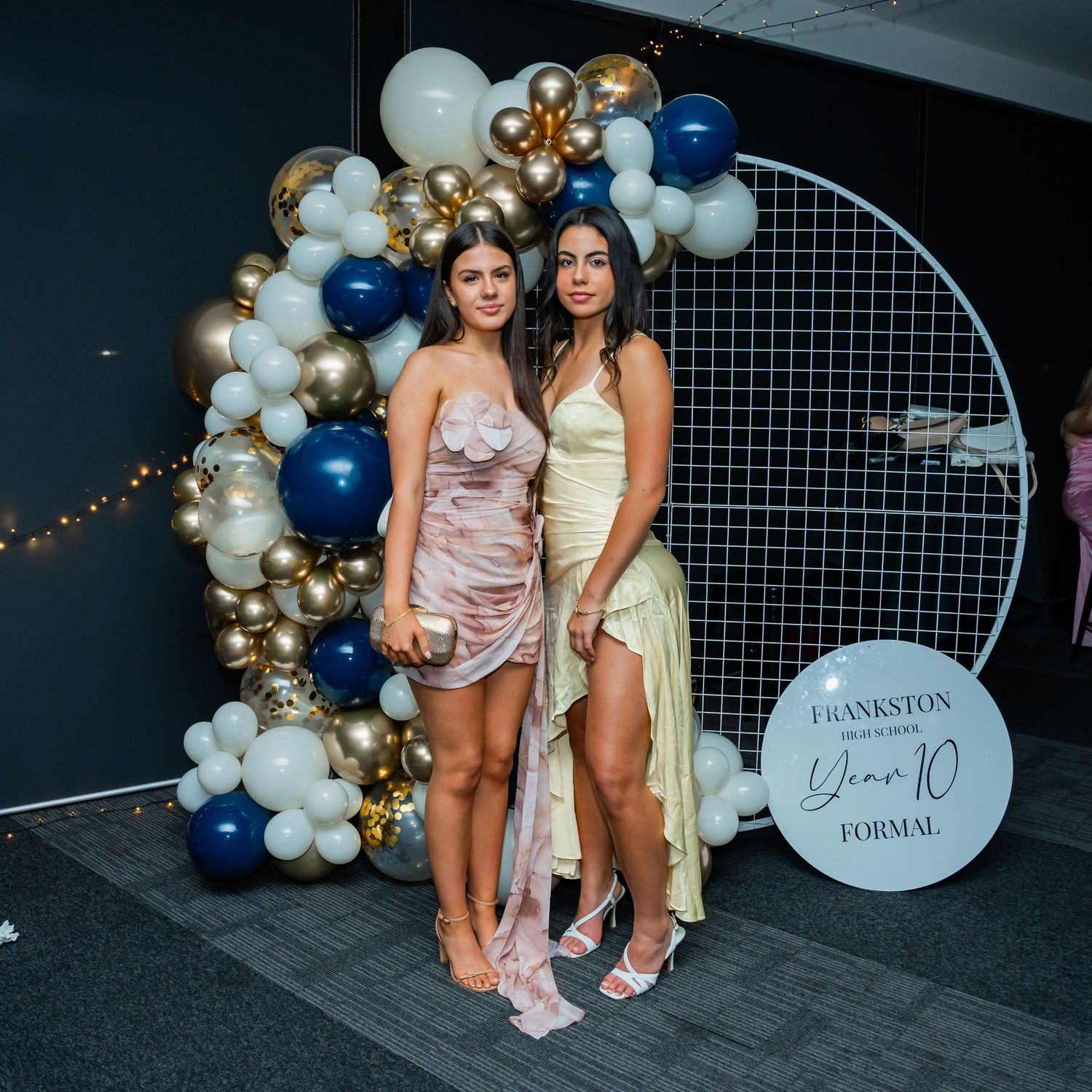 People pose by decorative balloon arch and formal signage at an elegant evening event with navy and gold accents.