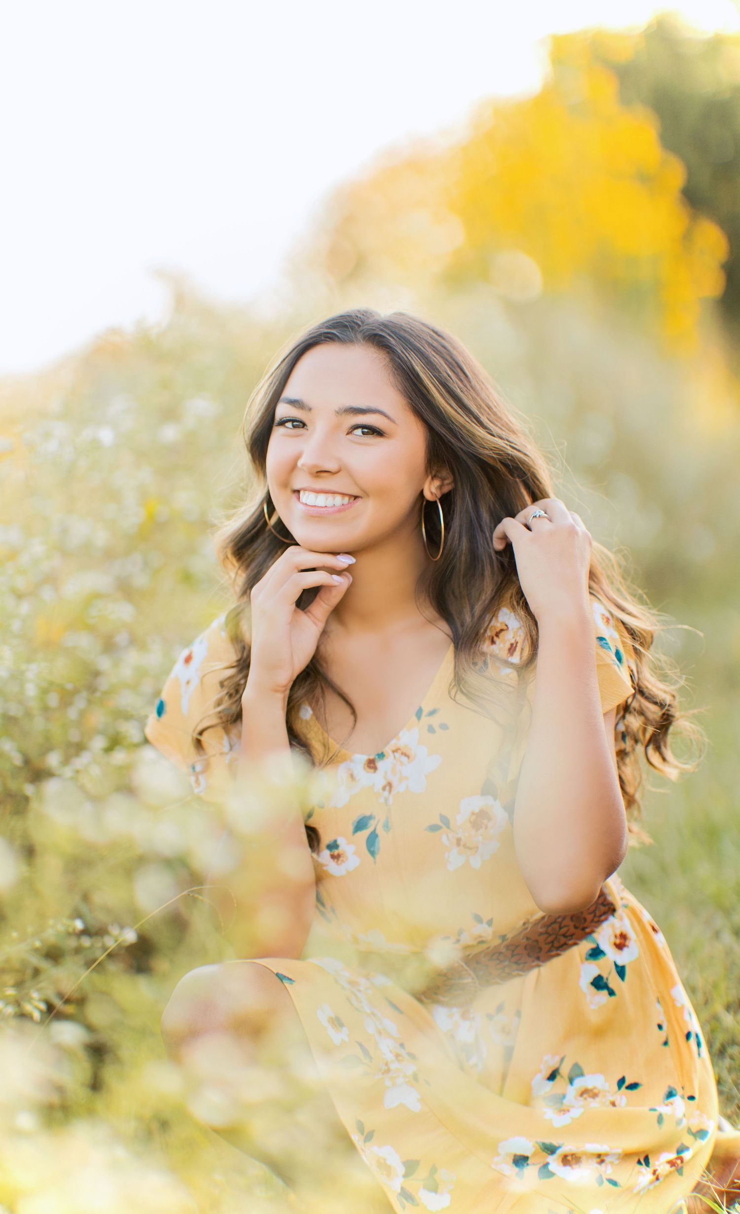 Senior girl smiling during a golden hour portrait session at Knoxville Botanical Garden, wearing a yellow floral dress in a field.