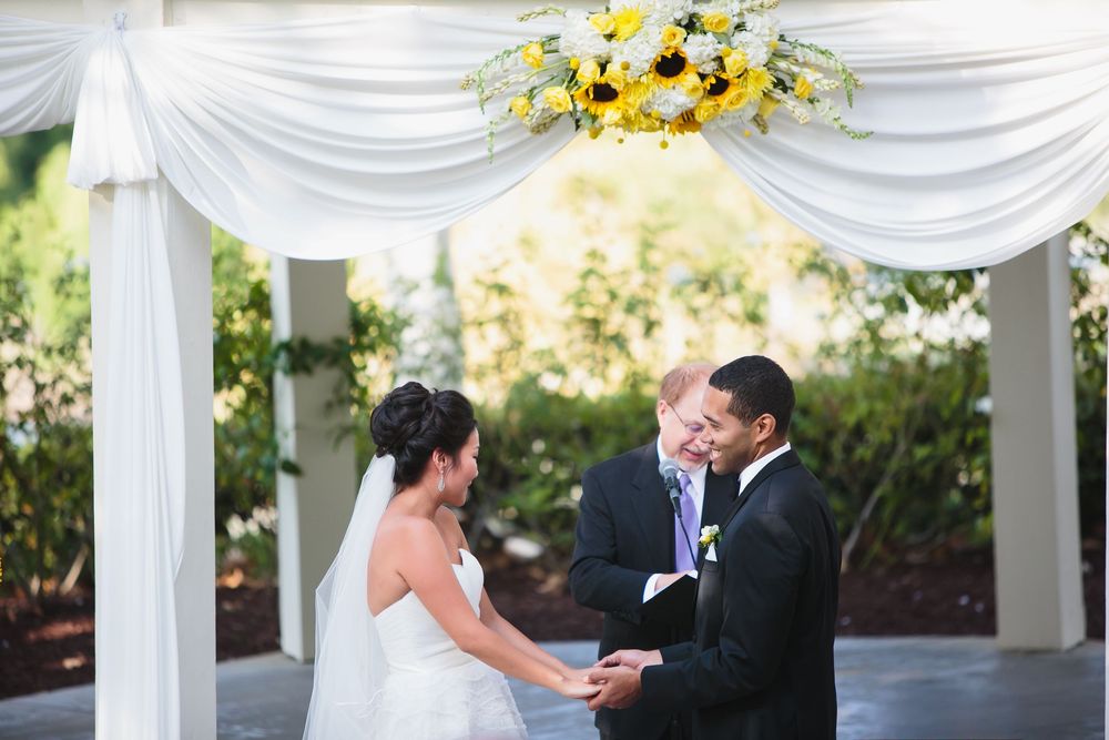 Wedding ceremony under white draped gazebo with floral sunflower arrangements.