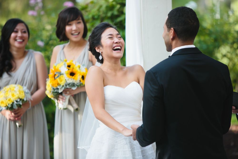 Wedding party members laugh together during an outdoor ceremony with sunflower accents.