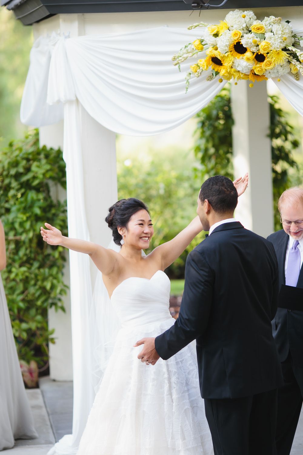 Couple celebrates during their wedding ceremony under white drapes and sunflower arrangements.