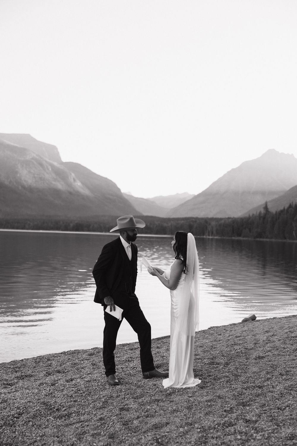 A couple shares an intimate moment by a serene mountain lake, with dramatic peaks in the background.