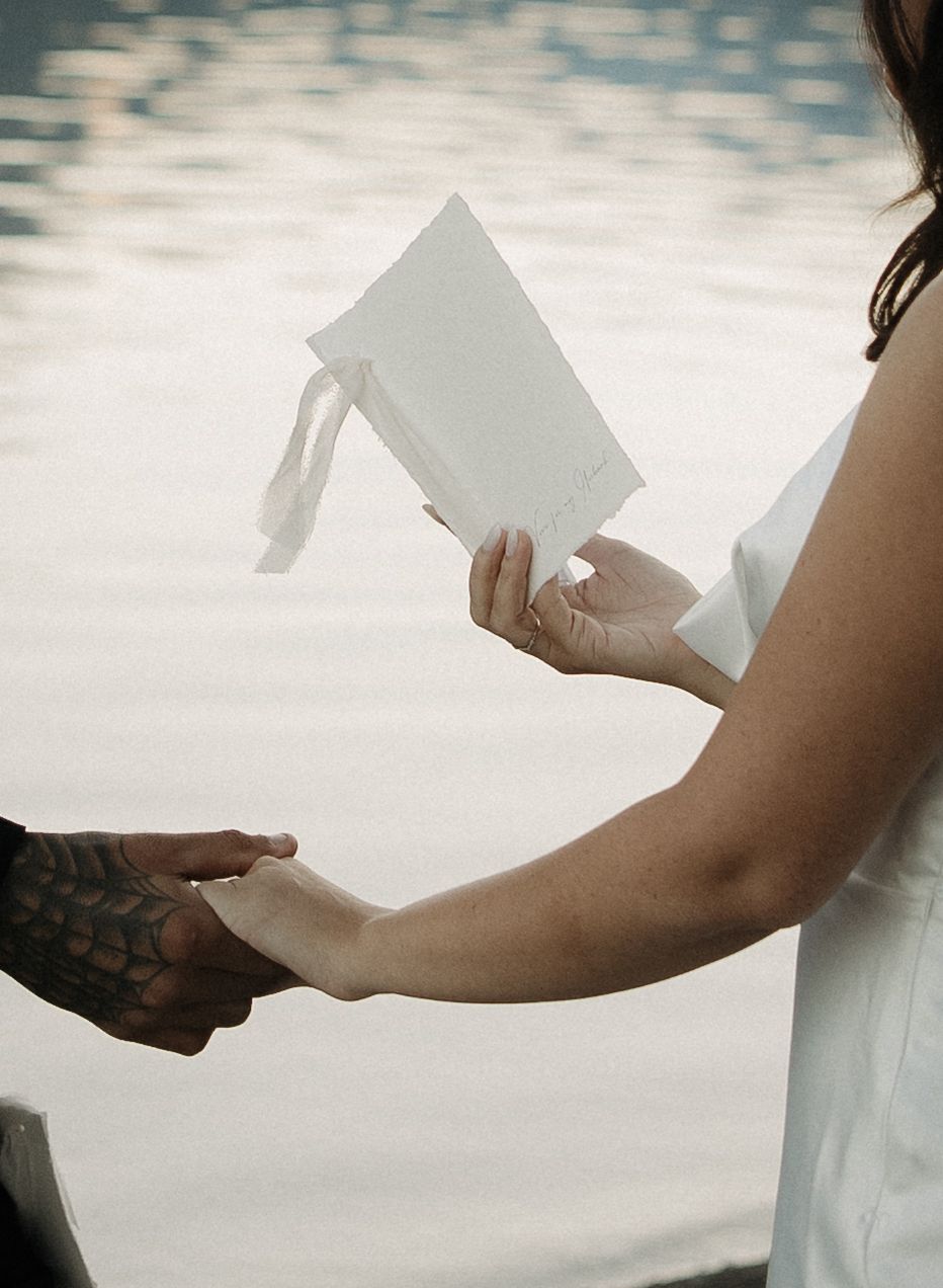 Hands holding a white paper or letter in a soft, romantic outdoor setting with dreamy bokeh lighting effects.