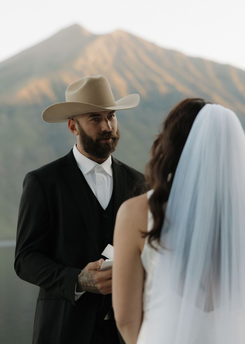 A bride and groom share an intimate moment in front of a scenic mountain landscape during their wedding ceremony.